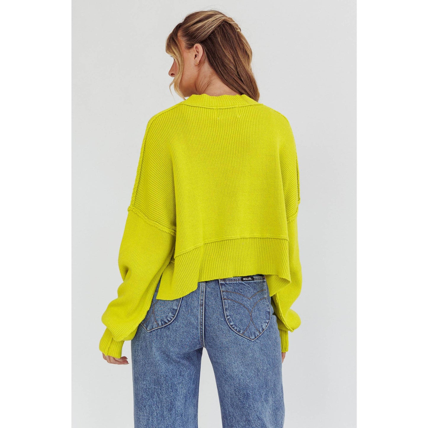 Person wearing a bright yellow sweater and blue jeans on a white background