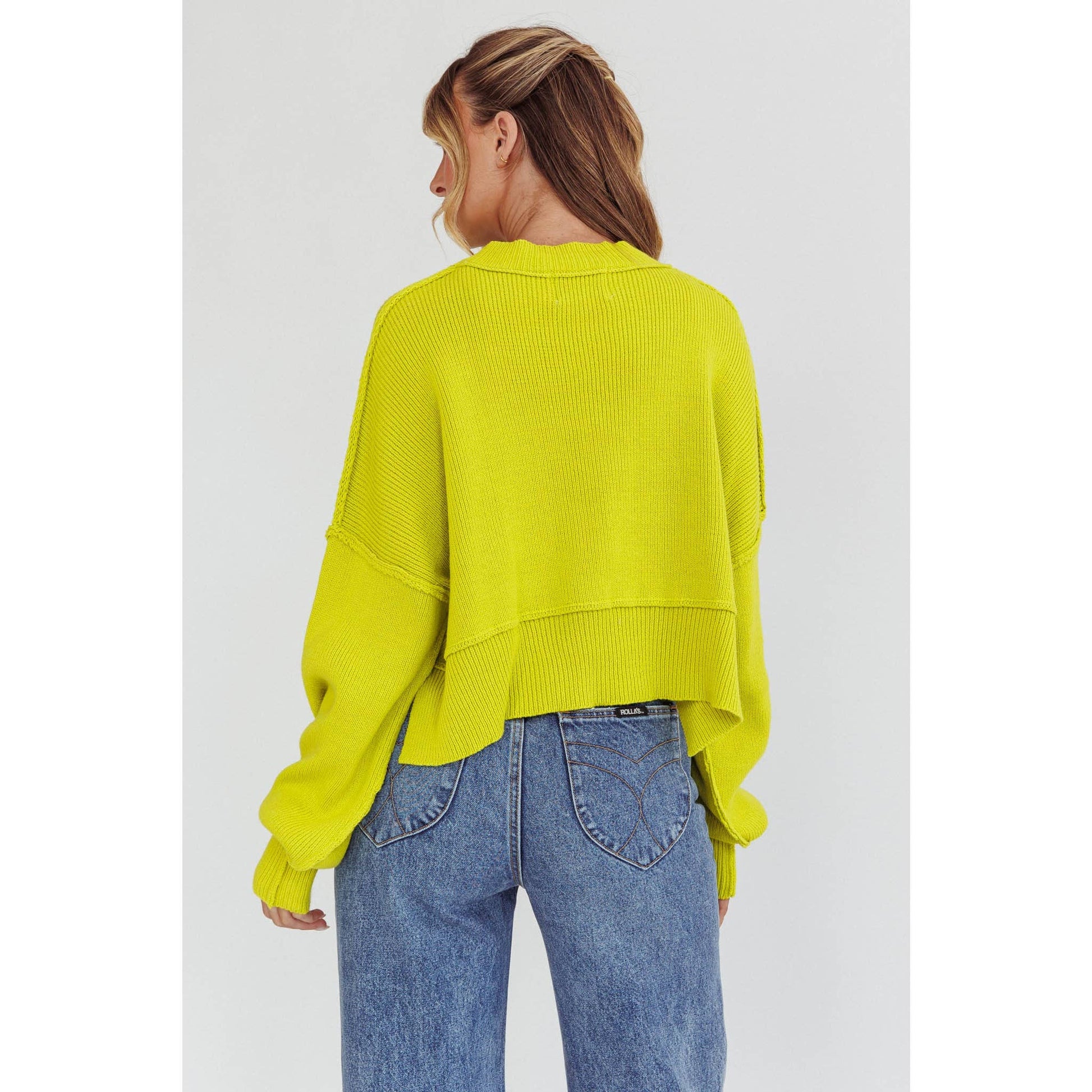 Person wearing a bright yellow sweater and blue jeans on a white background