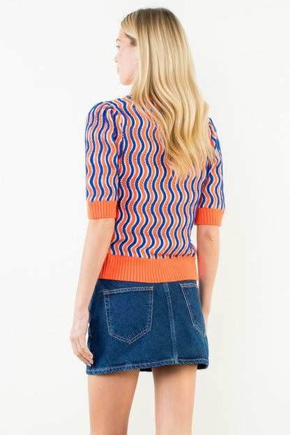 A woman shown from the back wearing a short-sleeve knit top with vertical wavy stripes in blue, orange, and white, paired with a blue denim mini skirt, against a plain white background.