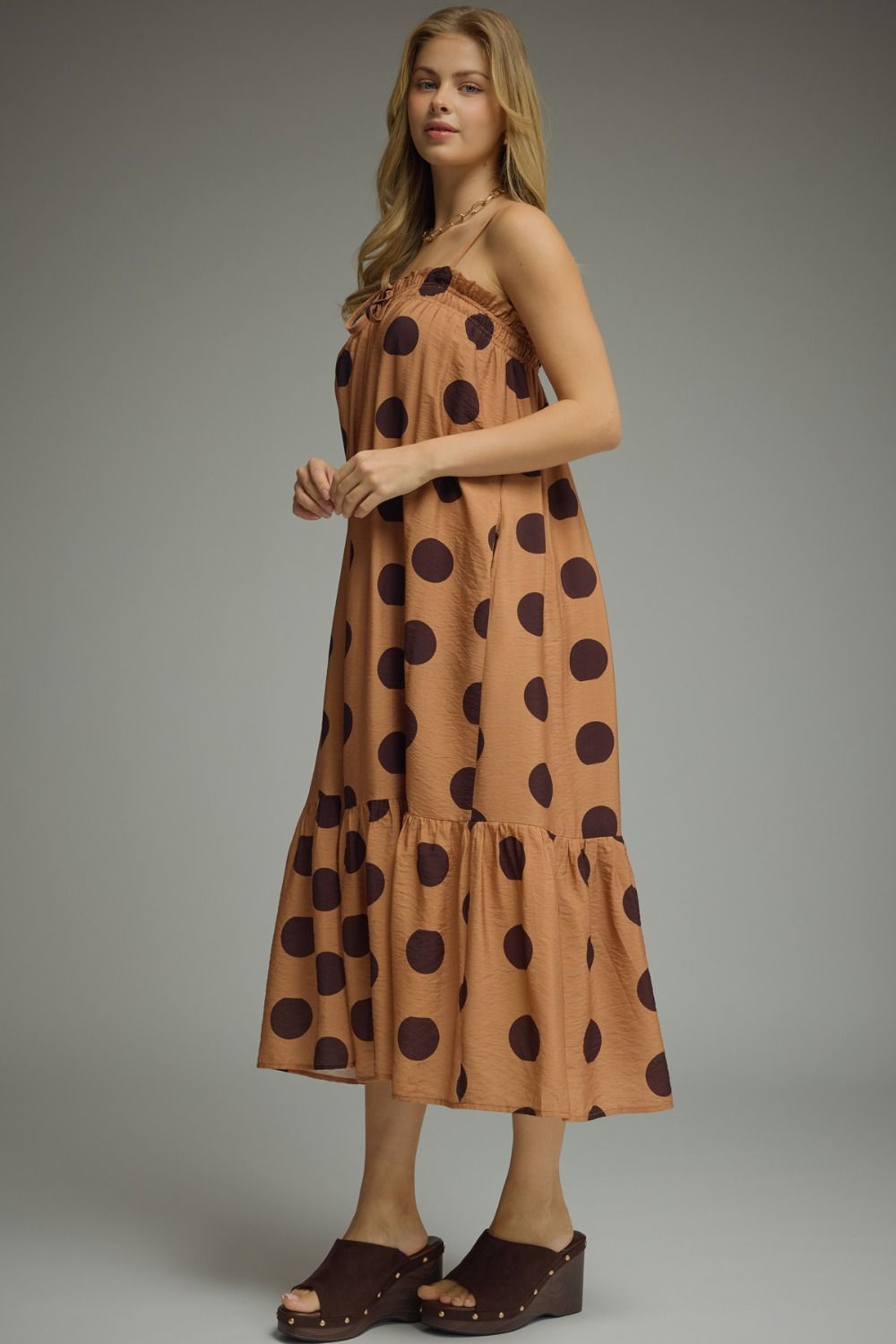 Woman wearing a brown dress with black polka dots against a gray background
