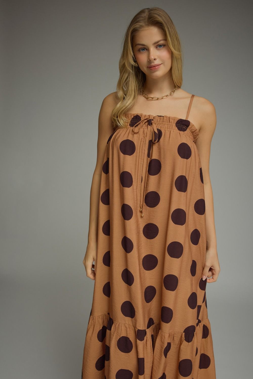 Woman wearing a brown dress with black polka dots against a gray background