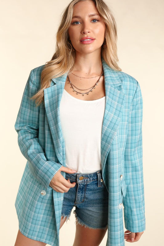 Woman wearing a turquoise plaid oversized blazer with a classic lapel collar, white button details, and cuffed sleeves.