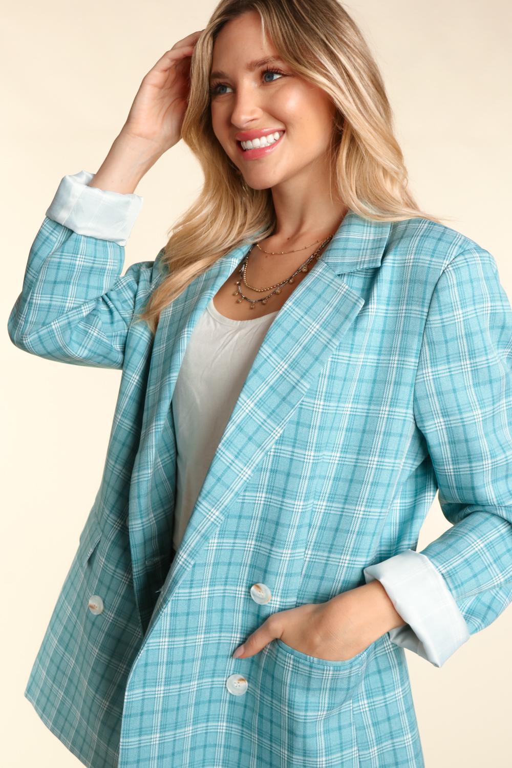 Woman wearing a turquoise plaid oversized blazer with a classic lapel collar, white button details, and cuffed sleeves.