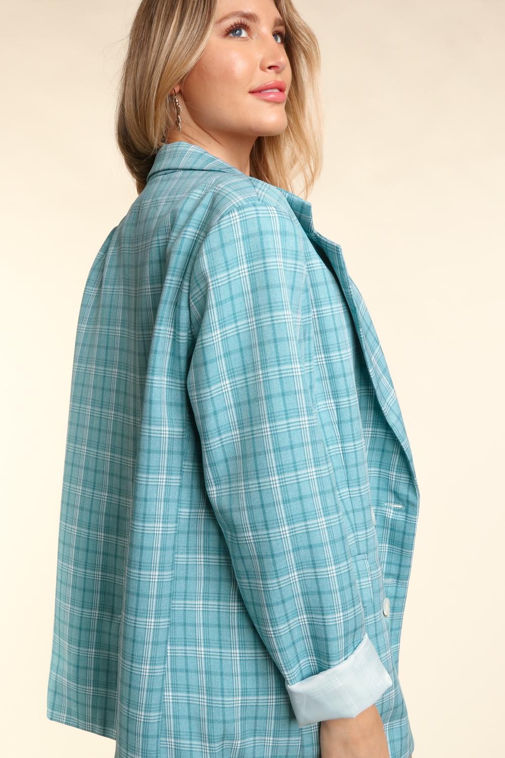 Woman wearing a turquoise plaid oversized blazer with a classic lapel collar, white button details, and cuffed sleeves.