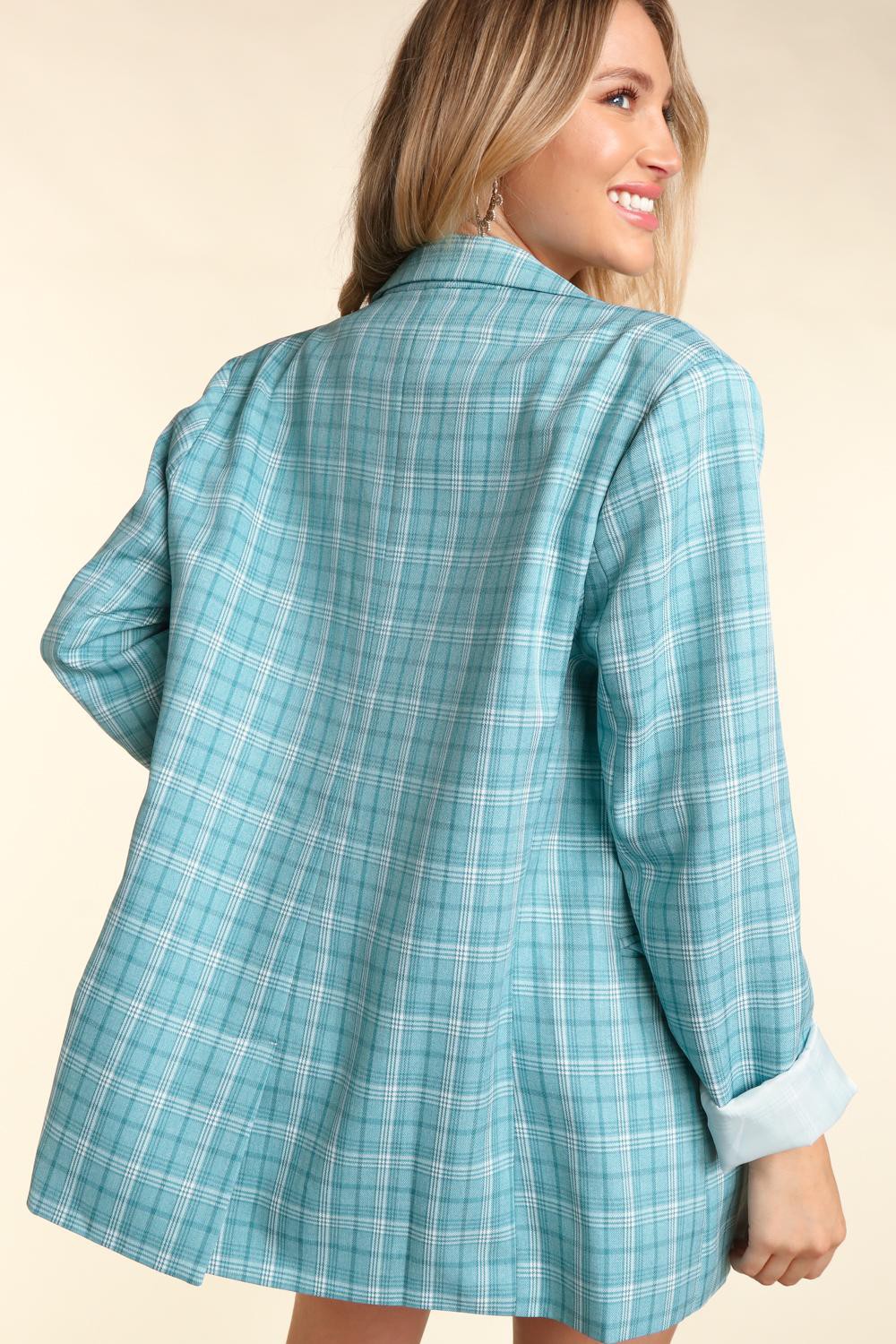 Woman wearing a turquoise plaid oversized blazer with a classic lapel collar, white button details, and cuffed sleeves.