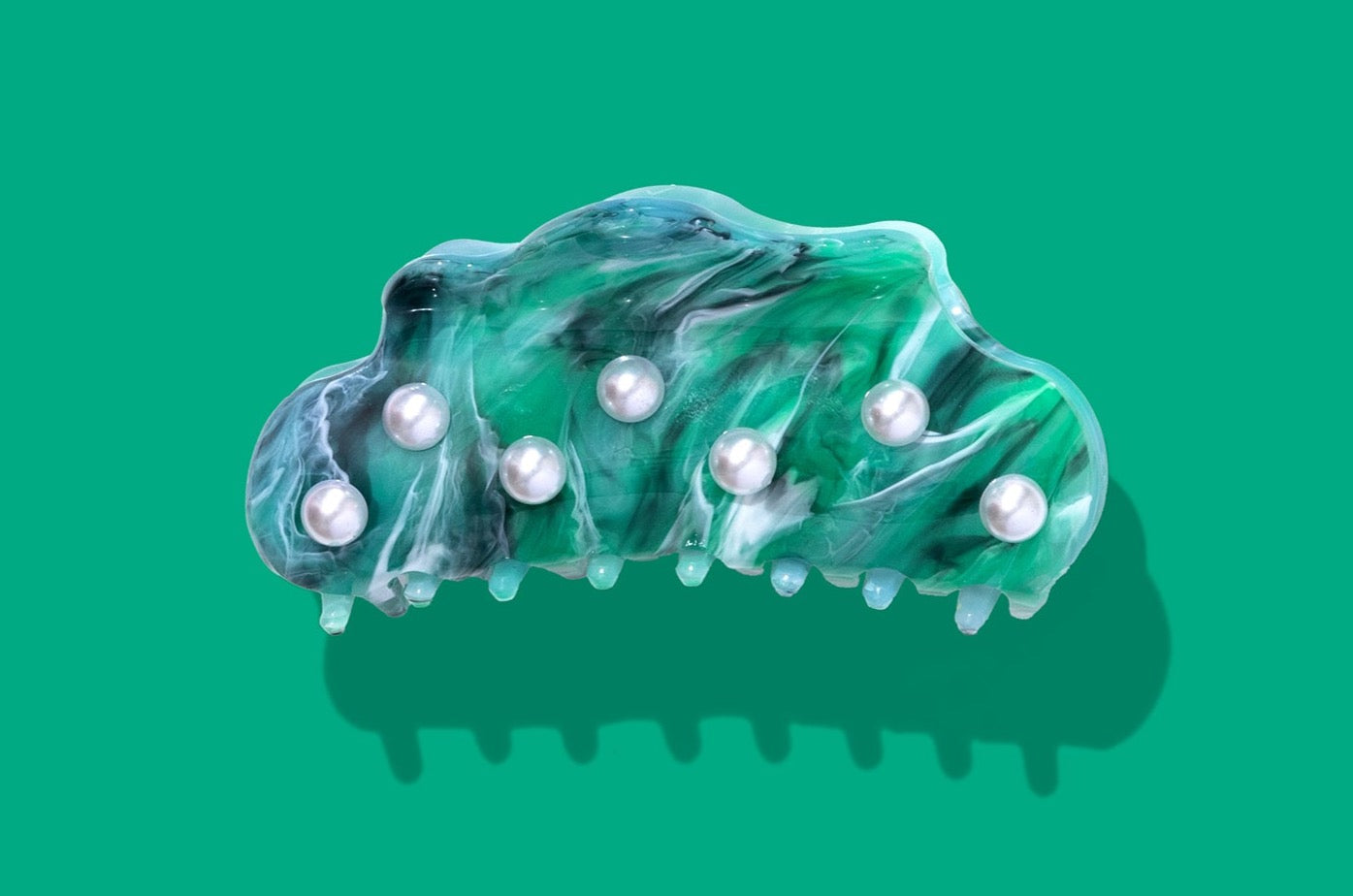 A translucent green and blue hair claw clip decorated with seven white faux pearls, shown against a solid green background with a soft drop shadow.