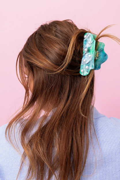 Long brown hair with a green hair clip against a pink background