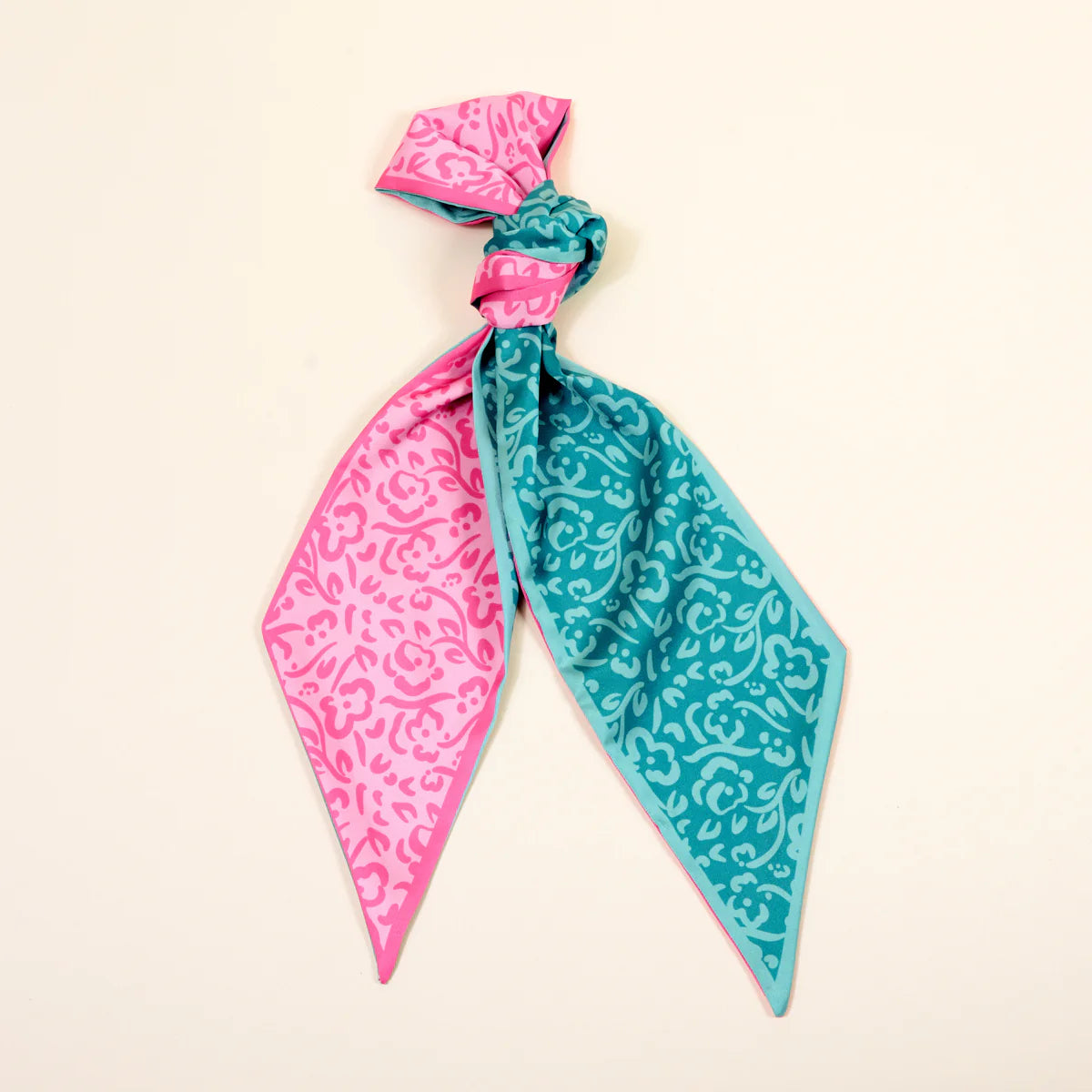 Two patterned scarves, one pink and one blue, tied together on a beige background.