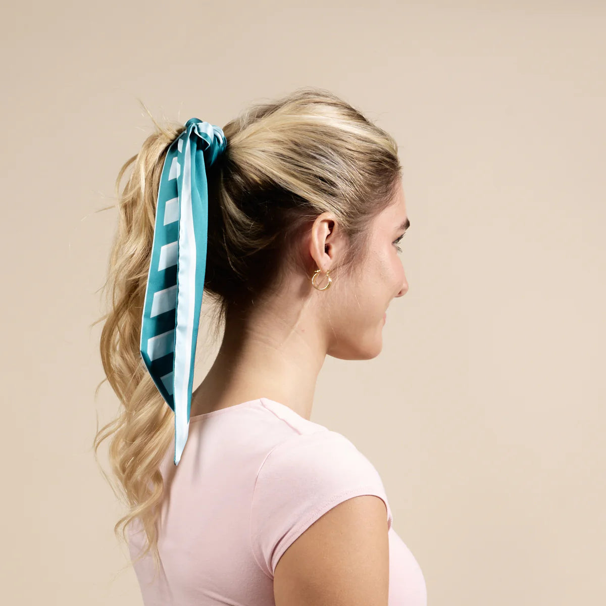 Woman with a teal and white striped hair tie in her ponytail against a beige background