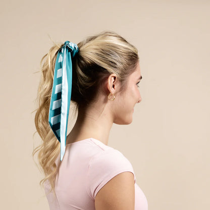 Woman with a teal and white striped hair tie in her ponytail against a beige background