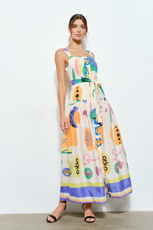 Woman wearing a colorful playful print maxi dress with belt and sandals, standing indoors