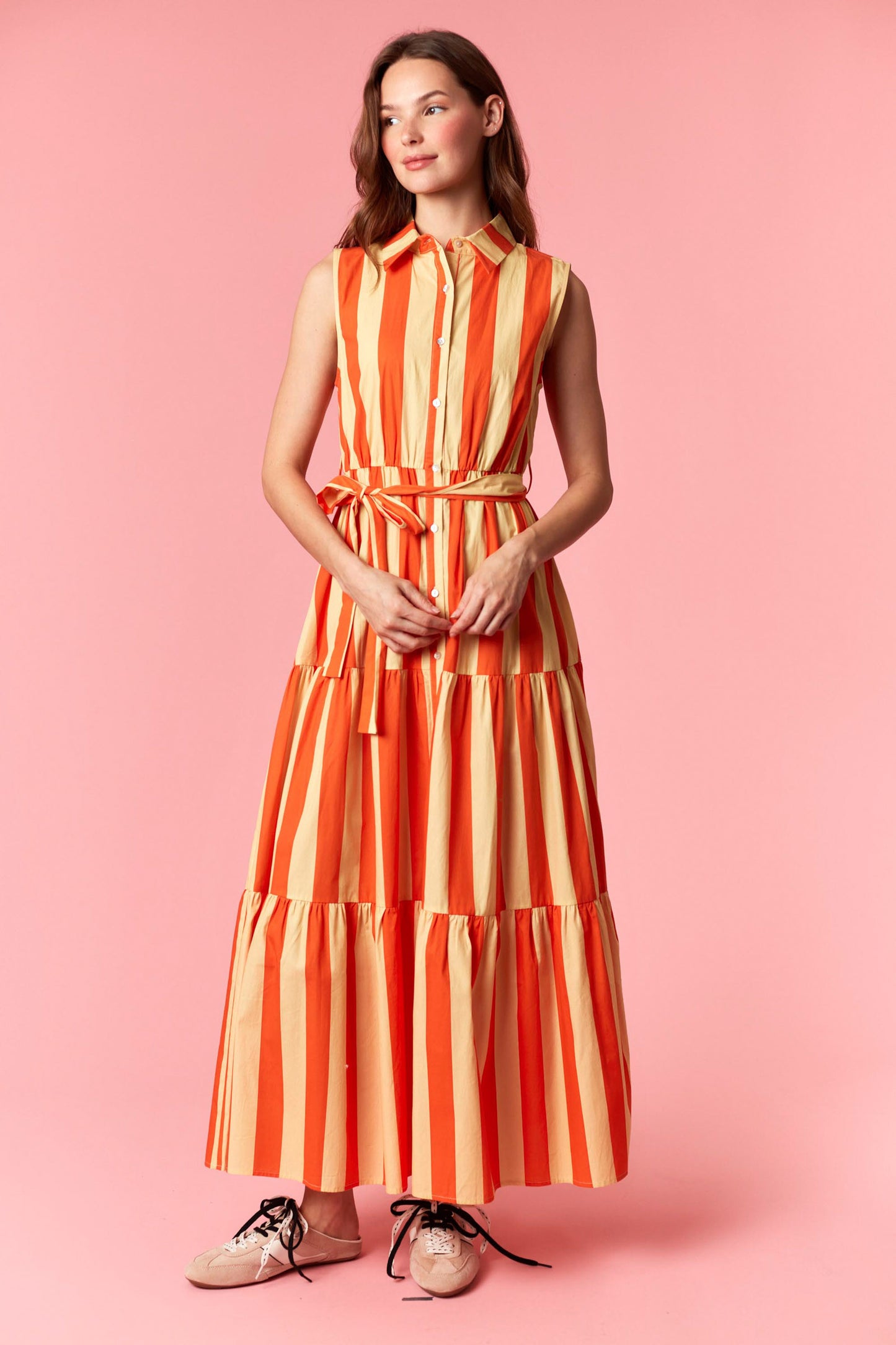 Woman wearing a orange and yellow striped dress on a pink background