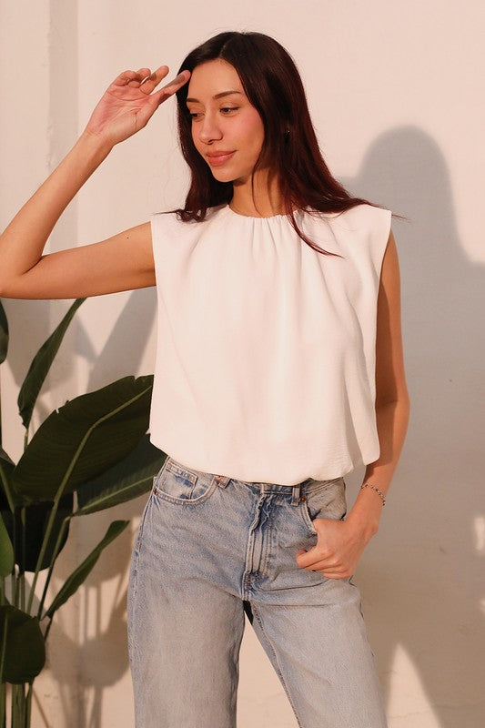 Woman wearing a white sleeveless top and light blue jeans against a neutral background