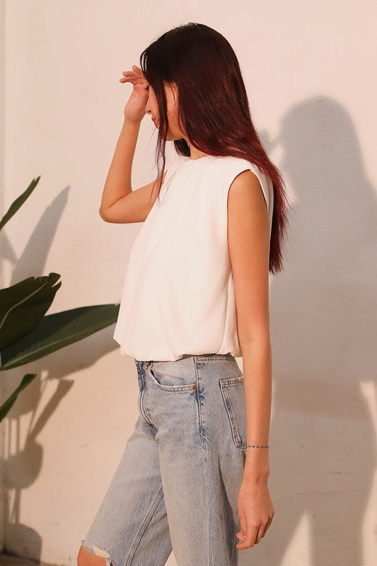 Person wearing a white sleeveless top and light blue jeans against a plain background