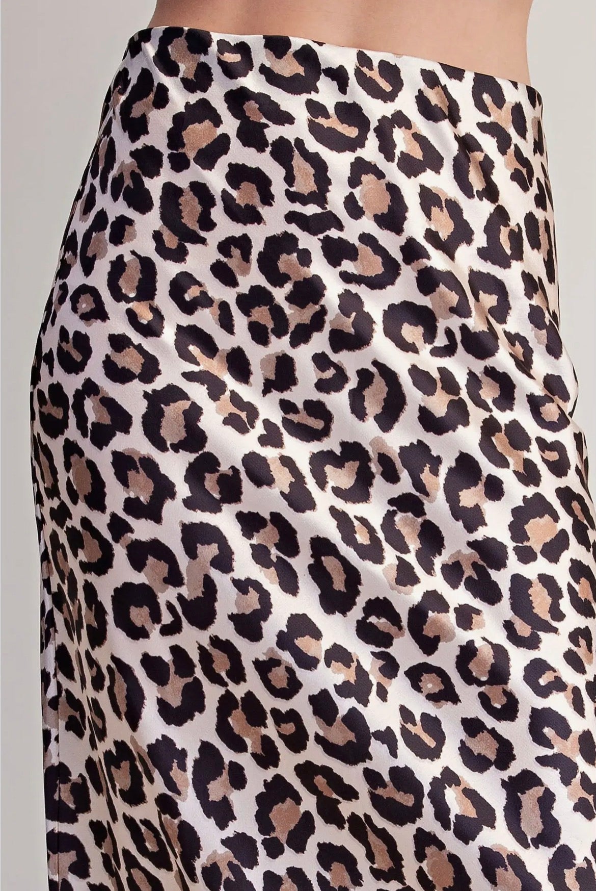 Close-up of a leopard print skirt with a cream base and black, brown, and beige spots, shown on a model.