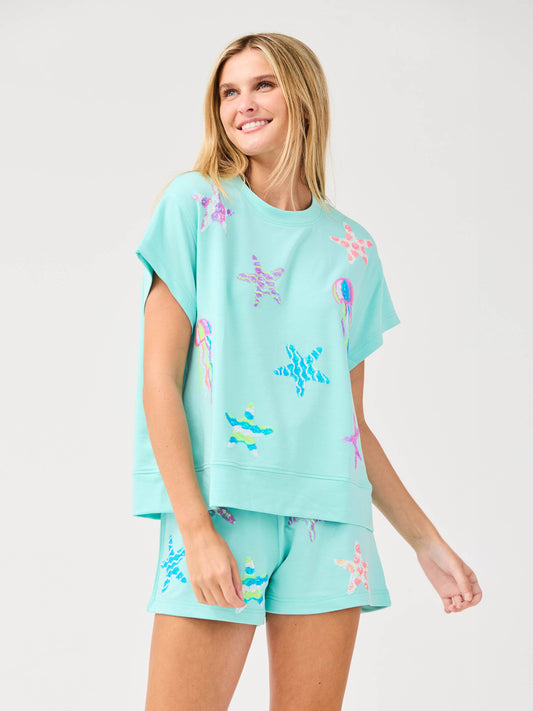 Woman wearing aqua blue matching top and shorts set with colorful starfish and sea-inspired prints