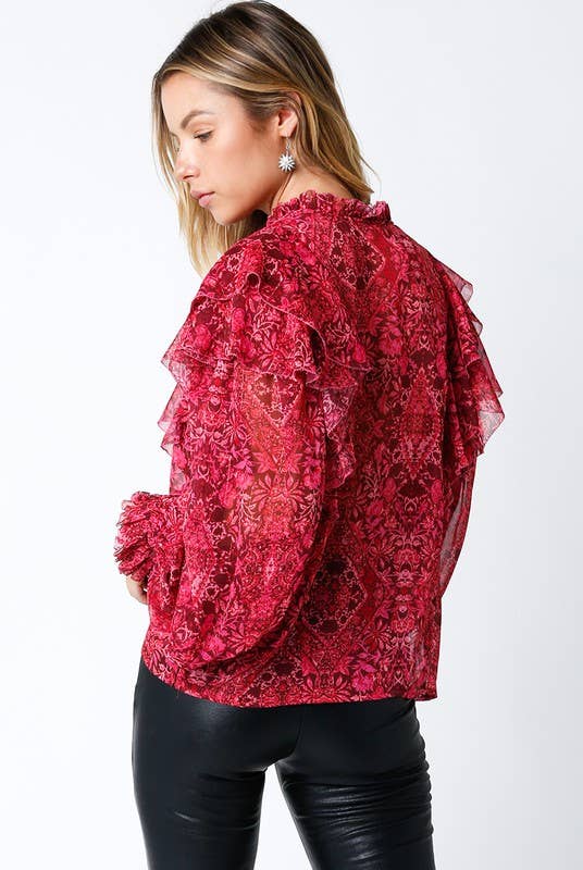 Woman wearing a red floral ruffled blouse with sheer sleeves and black faux leather pants.