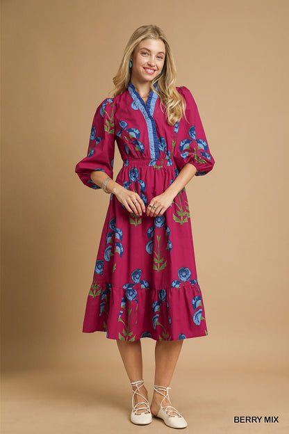 Model wearing a berry pink floral midi dress with blue trim neckline, puff sleeves, and tiered skirt — vibrant fall dress from Milo & Lily Boutique.