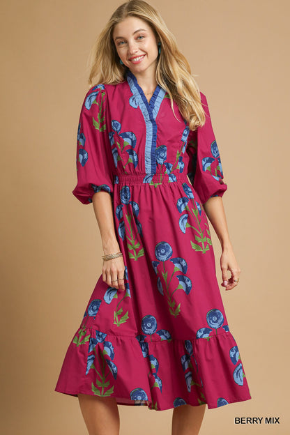 Model wearing a berry pink floral midi dress with blue trim neckline, puff sleeves, and tiered skirt — vibrant fall dress from Milo & Lily Boutique.