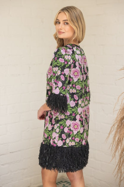 Back view of a model wearing a black jacquard mini dress with pink floral embroidery and black feather trim on the sleeves and hem — elegant statement party dress from Milo & Lily Boutique.