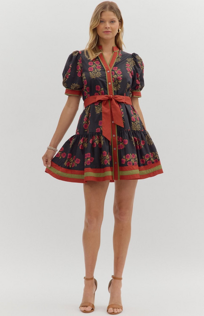 Model wearing a black floral mini dress with red sash belt, puff sleeves, and green trim detail — elegant button-down boutique dress from Milo & Lily Boutique.