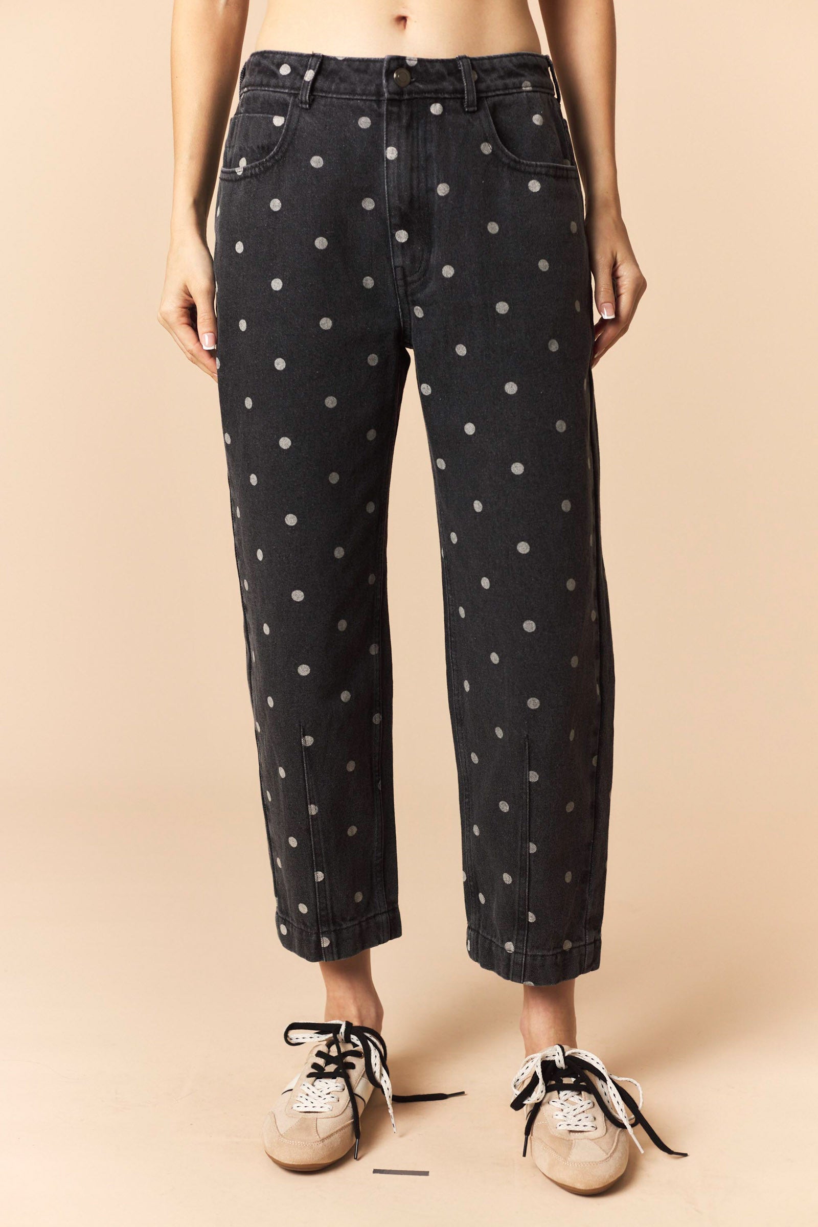 Person wearing black polka dot jeans on a beige background