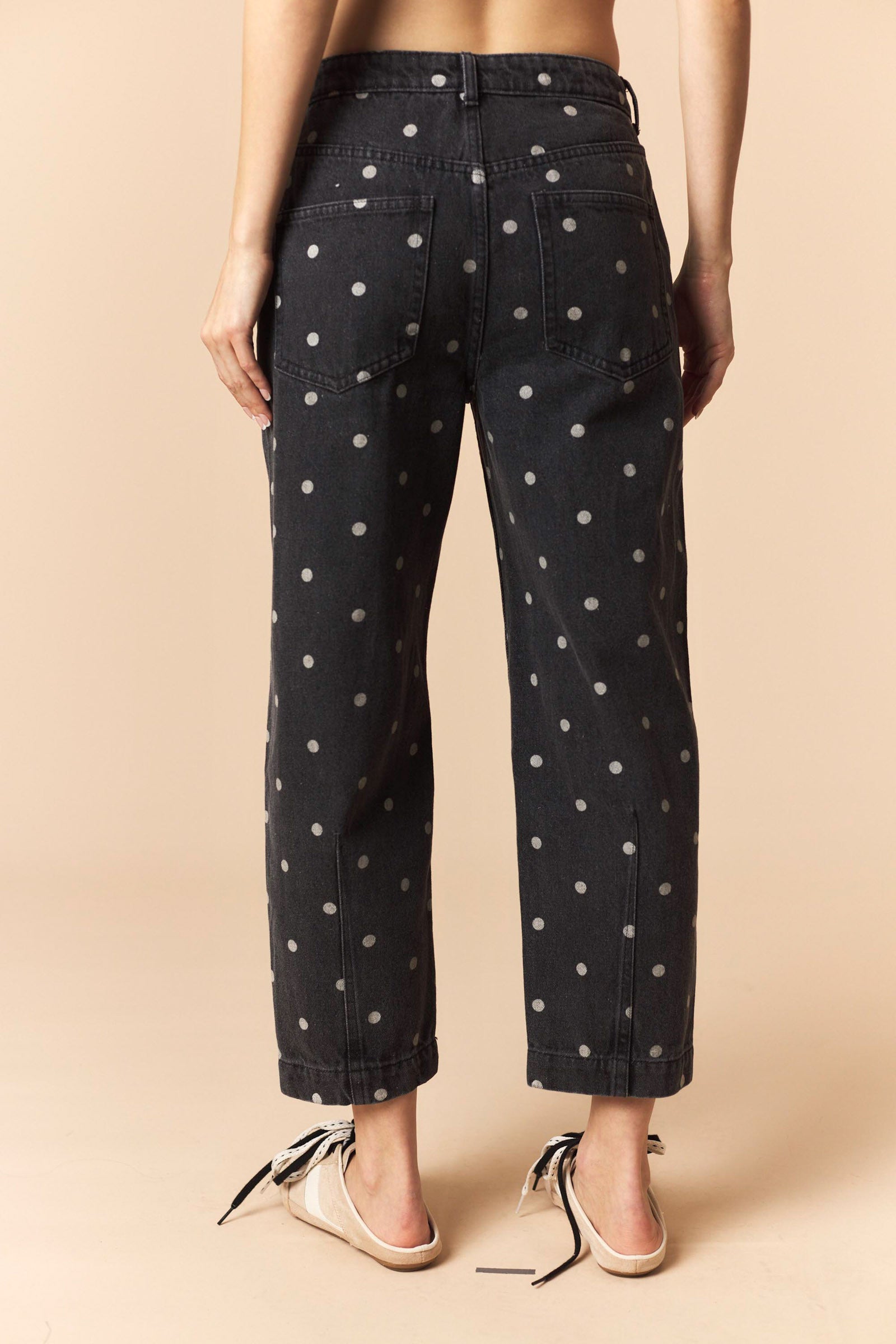 Person wearing black polka dot jeans on a beige background
