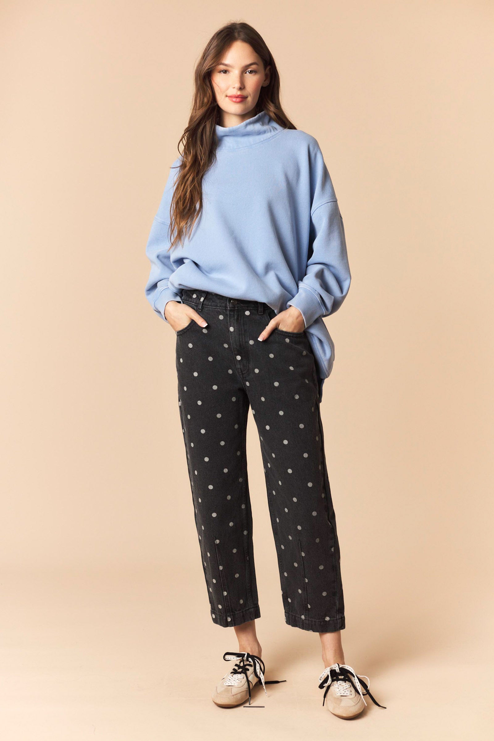 Woman wearing a blue sweater and black pants with white patterns on a beige background