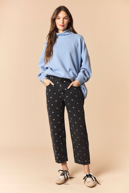 Woman wearing a blue sweater and black pants with white patterns on a beige background