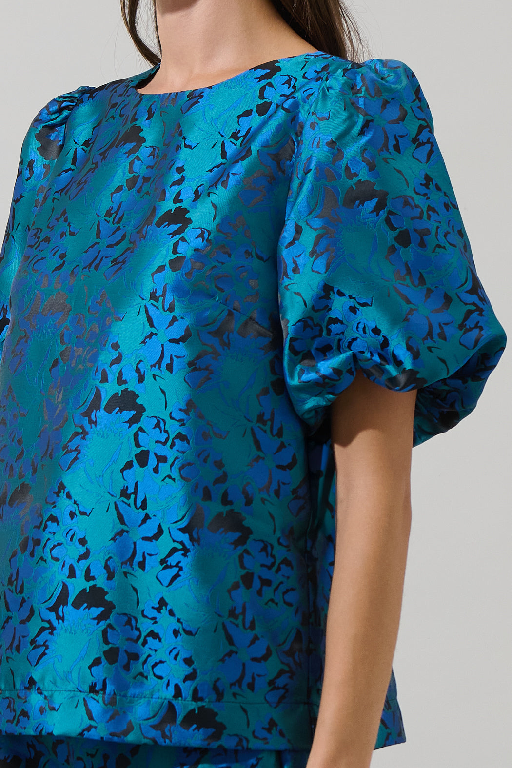Close-up of a teal blue jacquard puff sleeve top with a subtle metallic floral pattern — elegant and bold boutique blouse from Milo & Lily.