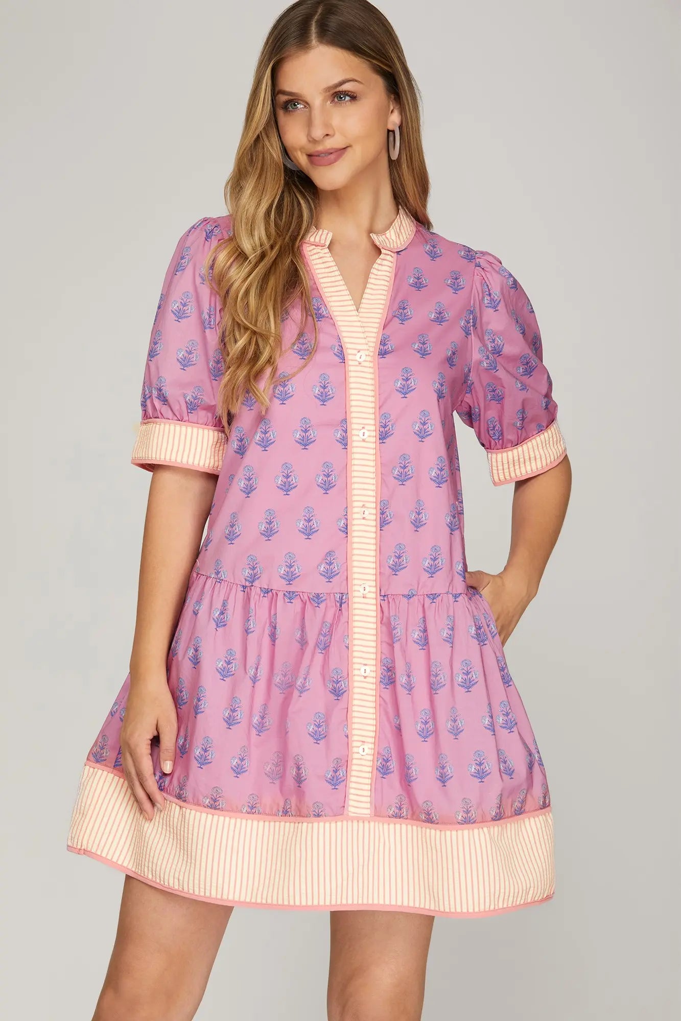 Woman wearing a pink dress with blue floral pattern on a gray background