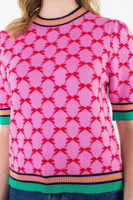 Close-up of pink and red patterned knit top with contrast ribbed collar and hem in green, yellow, and navy — colorful boutique style.