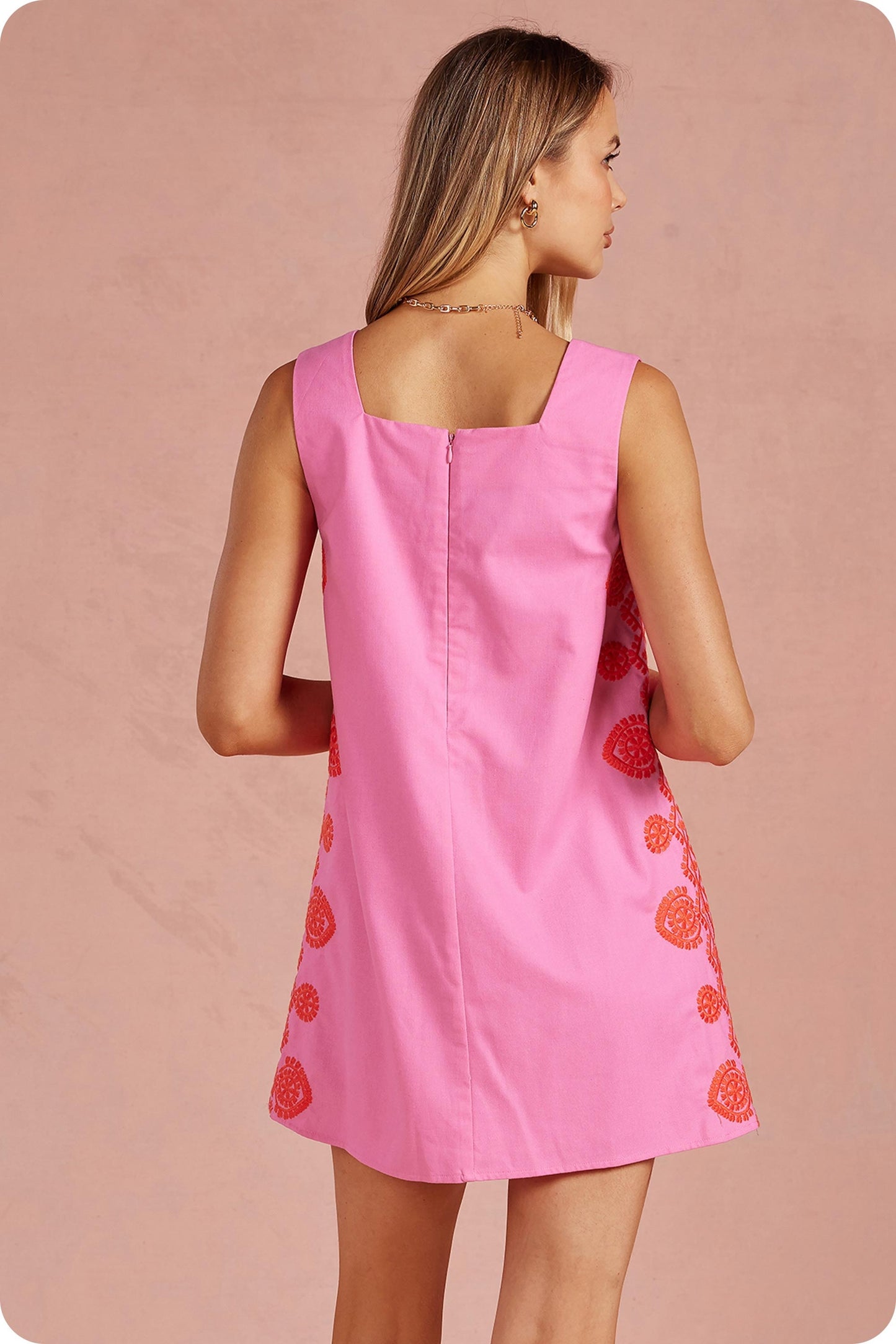 Woman wearing a pink dress with red floral patterns on a pink background