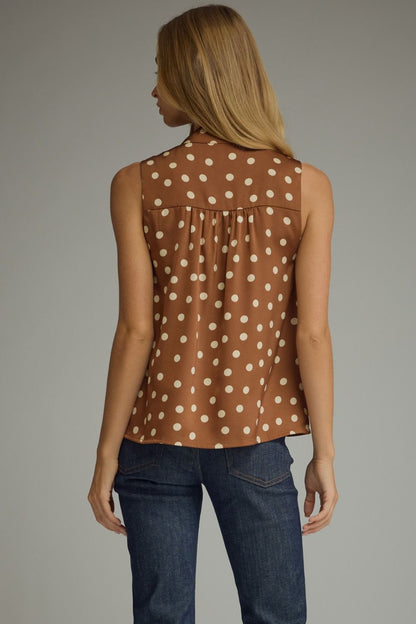 A woman shown from the back wearing a sleeveless brown top with a white polka dot pattern and dark blue jeans, photographed against a neutral gray studio background.