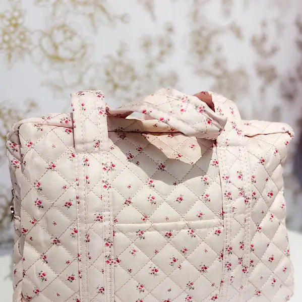 Quilted floral tote bag with pink rose print and handles, set against a patterned background