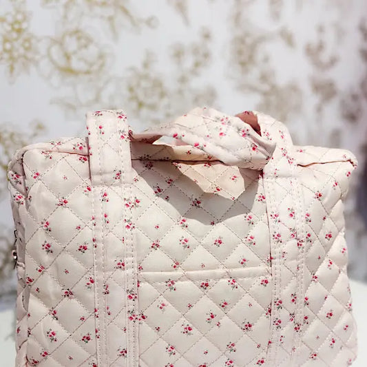 Quilted floral tote bag with pink rose print and handles, set against a patterned background