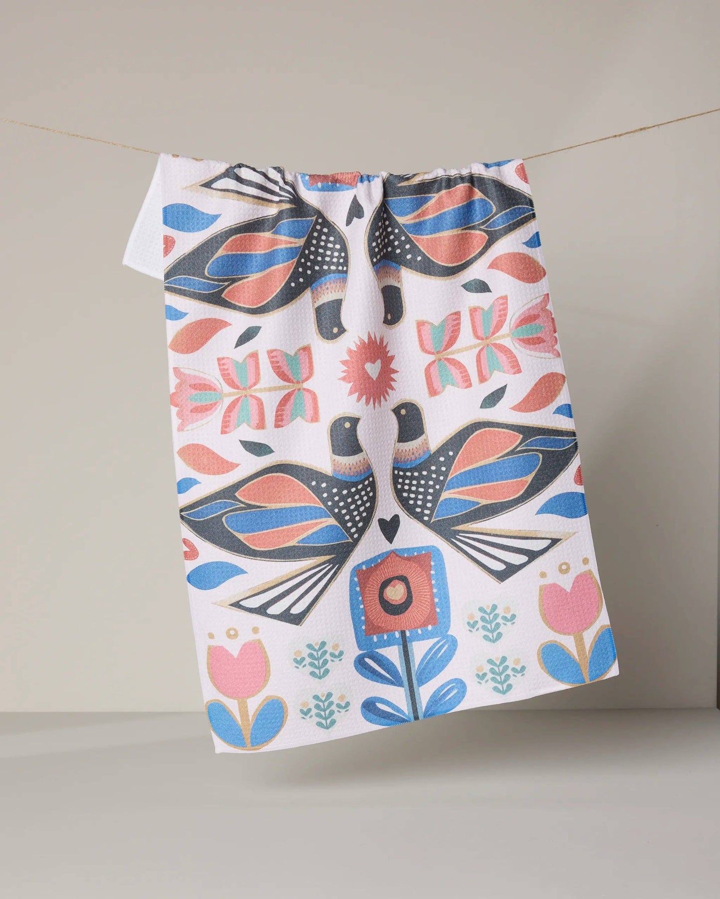 Colorful tea towel with folk art birds and floral pattern hanging on a neutral background