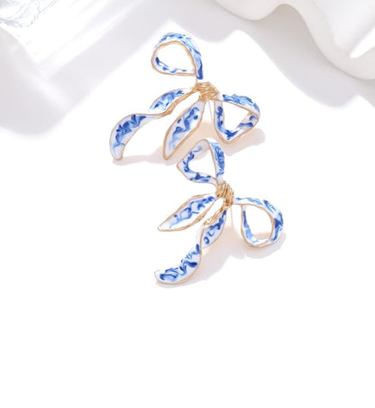 Blue and white enamel bow earrings with gold detailing, inspired by chinoiserie porcelain style — elegant and feminine accessory.