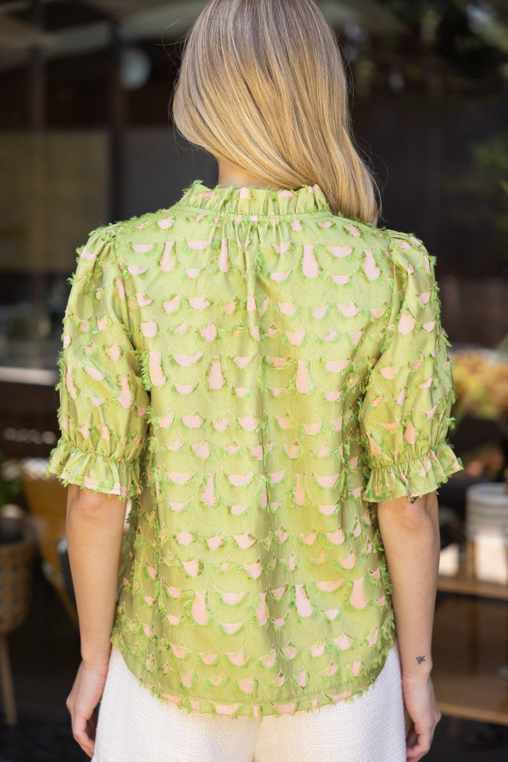 Back view of green and blush scallop-textured blouse with ruffled collar and short sleeves.