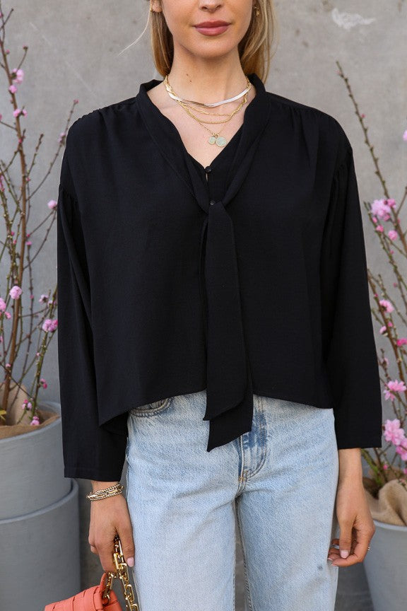 Model wearing black tie-neck blouse with long sleeves and relaxed fit—front view
