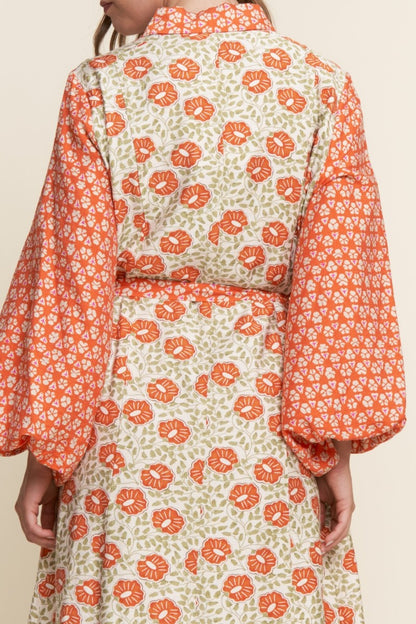 Person wearing a floral dress with orange and green pattern on a beige background