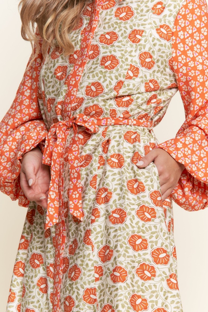Woman wearing a floral dress with orange and green pattern on a beige background