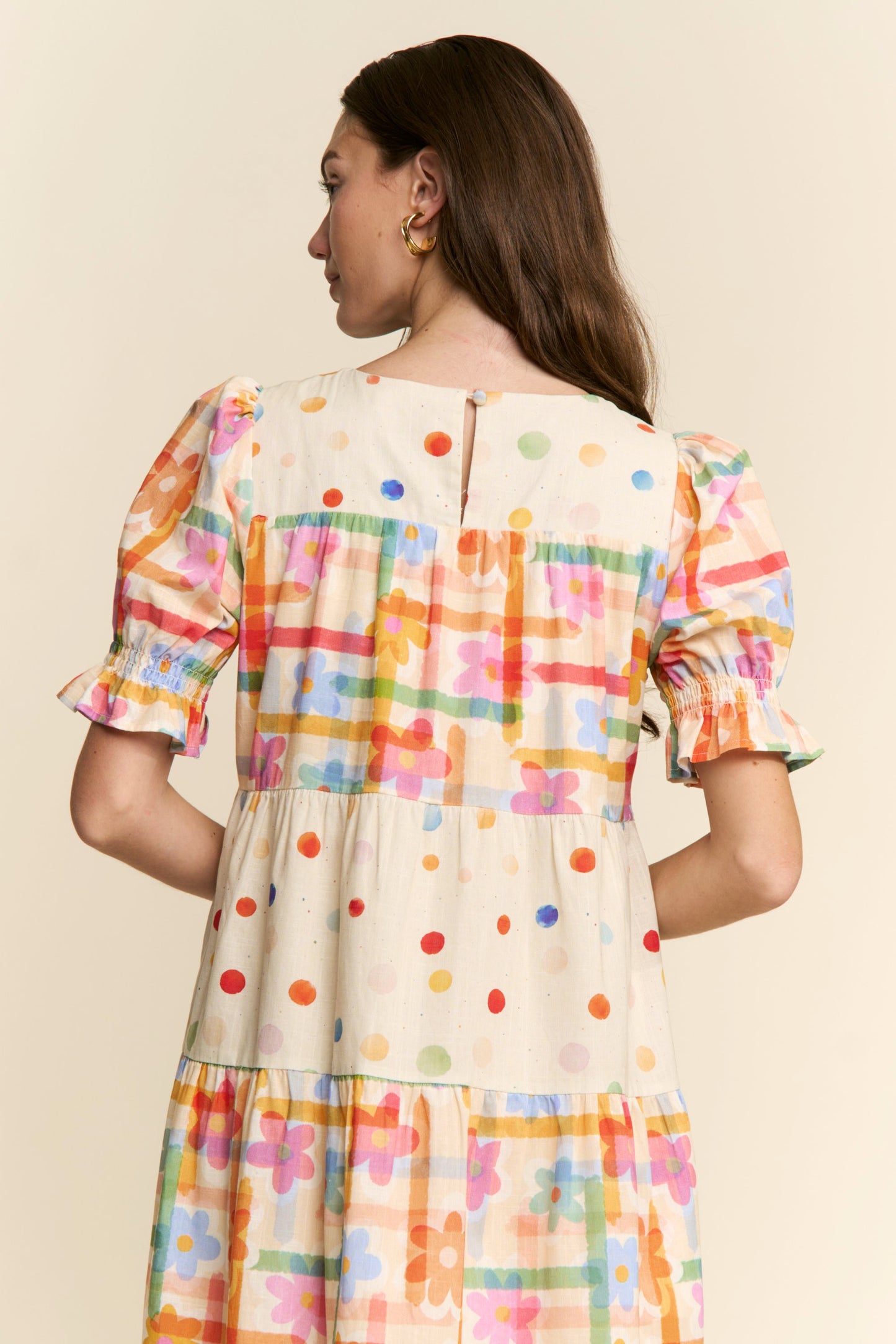 Woman wearing a colorful dress with a pattern of dots and geometric shapes on a beige background