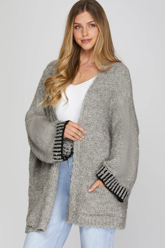 Woman wearing a gray cardigan with black patterned cuffs on a light gray background