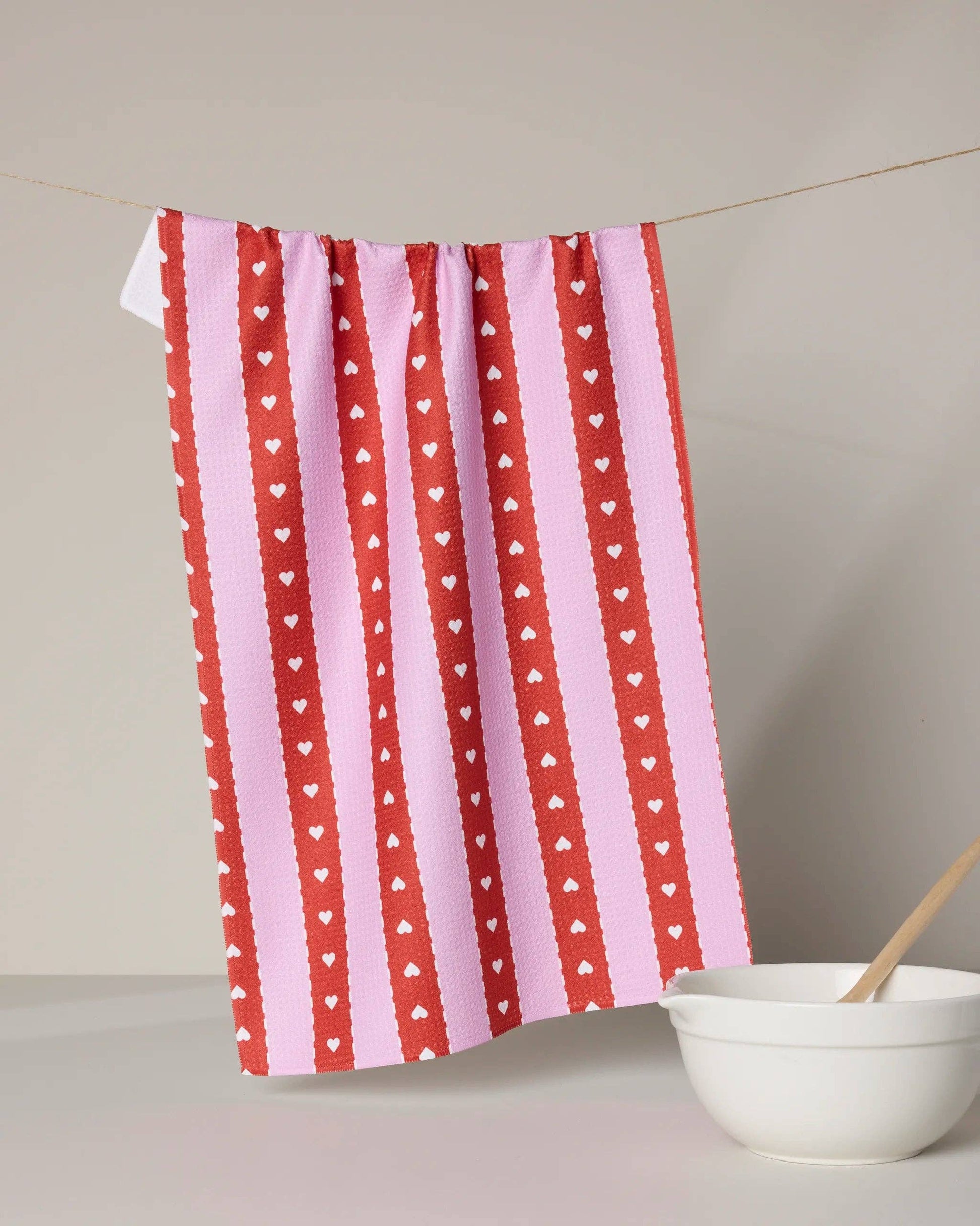 Red and pink striped kitchen towel with white heart pattern hanging near a white mixing bowl.