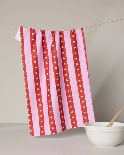 Red and pink striped kitchen towel with white heart pattern hanging near a white mixing bowl.
