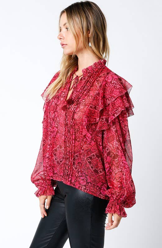 Woman wearing a sheer red floral ruffle blouse with long sleeves and black pants