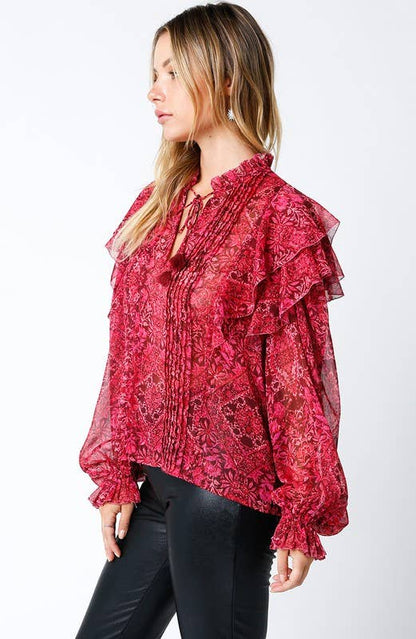 Woman wearing a sheer red floral ruffle blouse with long sleeves and black pants