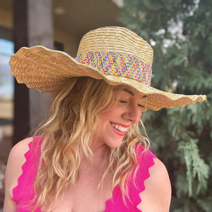 Woman in a pink top wearing a wide-brimmed straw sun hat with colorful band outdoors