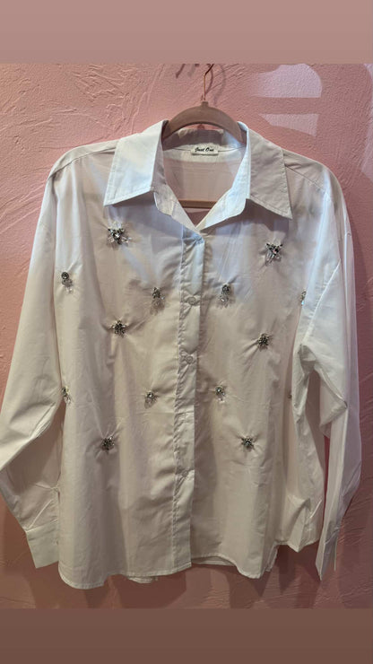 White embellished shirt featuring scattered rhinestone and beaded jewel appliqués, hung on blush pink background at Milo & Lily Boutique.